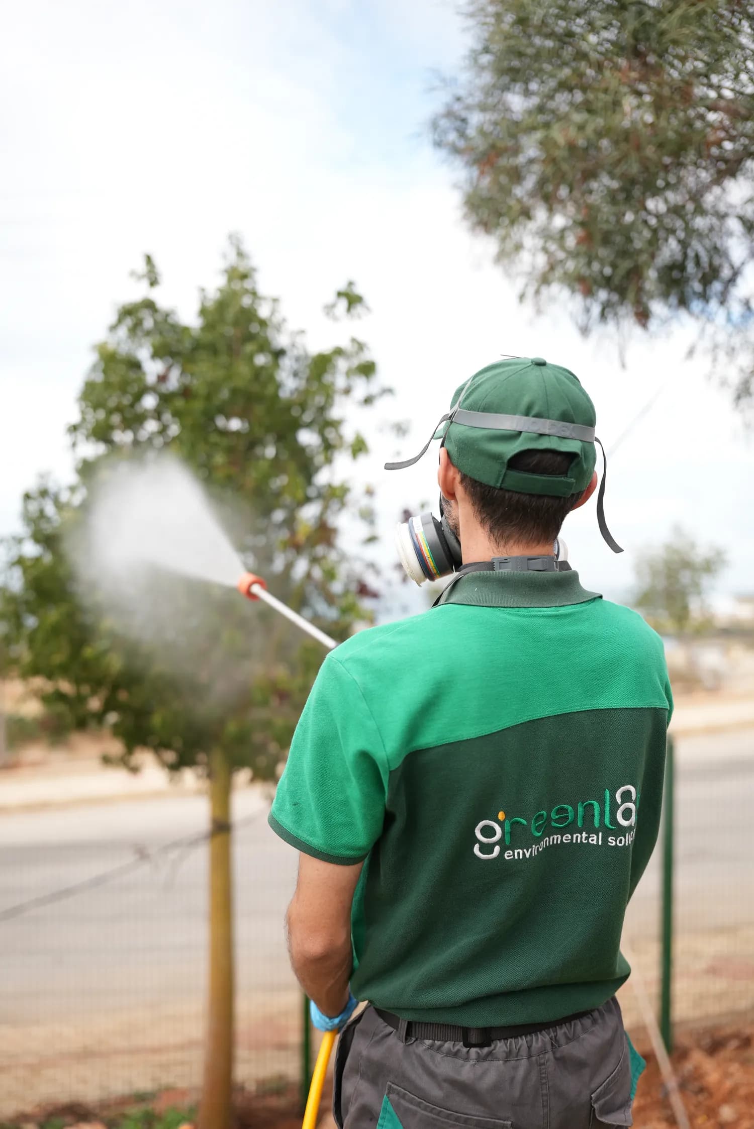 GreenLab technician applying an exterior pest treatment near a property boundary.